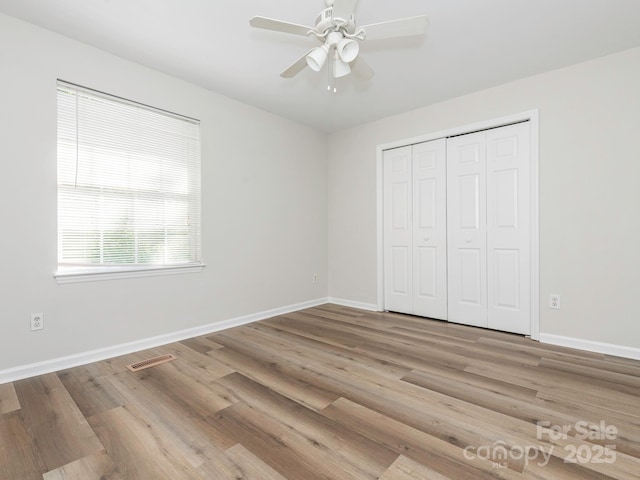 unfurnished bedroom with wood finished floors, baseboards, a closet, and visible vents