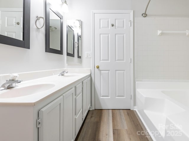bathroom featuring double vanity,  shower combination, a sink, and wood finished floors