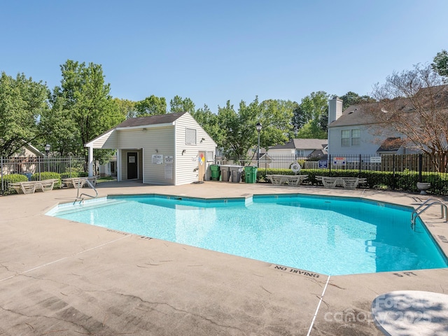 community pool featuring a patio area, fence, and an outbuilding