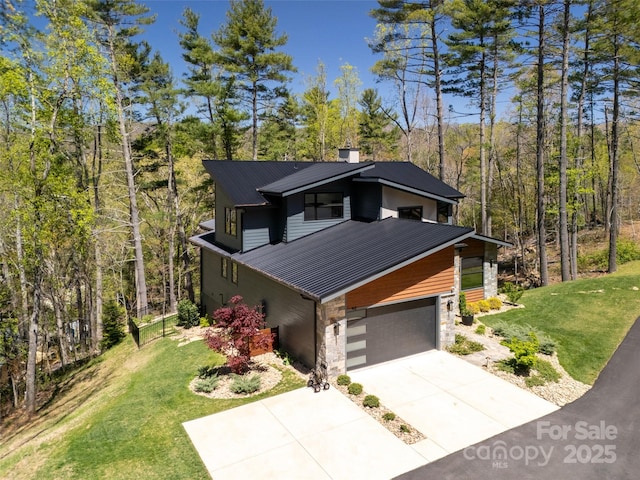 view of front of property with a wooded view, metal roof, driveway, stone siding, and a front yard