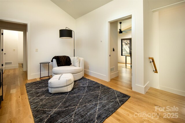 living area featuring visible vents, light wood-style floors, and vaulted ceiling