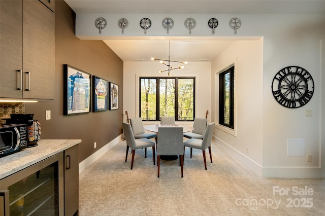 dining space featuring an inviting chandelier, beverage cooler, light colored carpet, and baseboards
