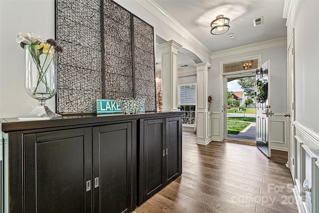 entrance foyer with visible vents, ornamental molding, decorative columns, a wainscoted wall, and dark wood finished floors