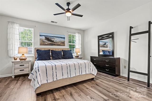 bedroom featuring baseboards, visible vents, multiple windows, and wood finished floors