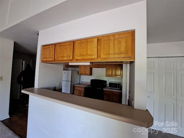 2527 Carya Pond Ln, Charlotte, NC 28212 - kitchen with black range with gas stovetop, built in study area, a peninsula, freestanding refrigerator, and brown cabinets