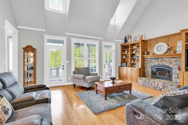 living area featuring a fireplace, light wood-type flooring, a healthy amount of sunlight, and high vaulted ceiling