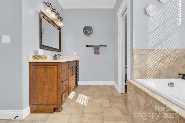 bathroom featuring stone tile floors, vanity, ornamental molding, a relaxing tiled tub, and baseboards