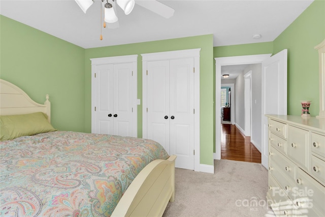 bedroom featuring two closets, ceiling fan, baseboards, and carpet