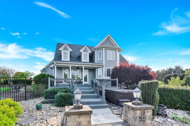 view of front facade featuring a shingled roof, fence, a hot tub, a porch, and ceiling fan