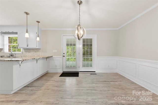 kitchen with a sink, a wainscoted wall, a breakfast bar, decorative light fixtures, and light wood finished floors