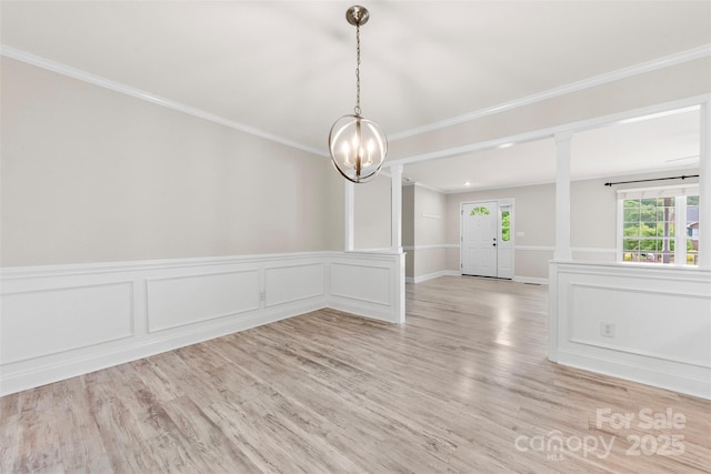 unfurnished dining area featuring a chandelier, crown molding, a decorative wall, and light wood-type flooring