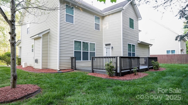 rear view of house featuring fence, a deck, and a lawn