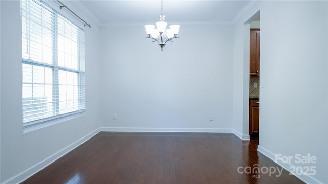spare room with a wealth of natural light, dark wood-style floors, and an inviting chandelier