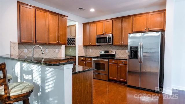 kitchen with a peninsula, visible vents, brown cabinetry, and appliances with stainless steel finishes