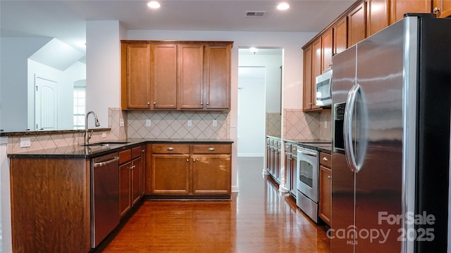 kitchen with dark wood finished floors, a peninsula, visible vents, a sink, and stainless steel appliances