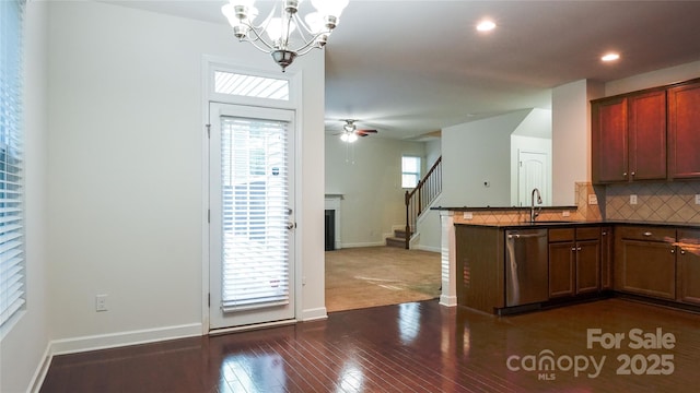kitchen featuring stainless steel dishwasher, a fireplace, a sink, dark countertops, and decorative backsplash