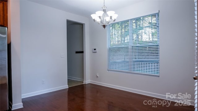 unfurnished dining area featuring baseboards, an inviting chandelier, and dark wood finished floors