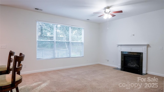 unfurnished living room featuring visible vents, baseboards, ceiling fan, light colored carpet, and a premium fireplace