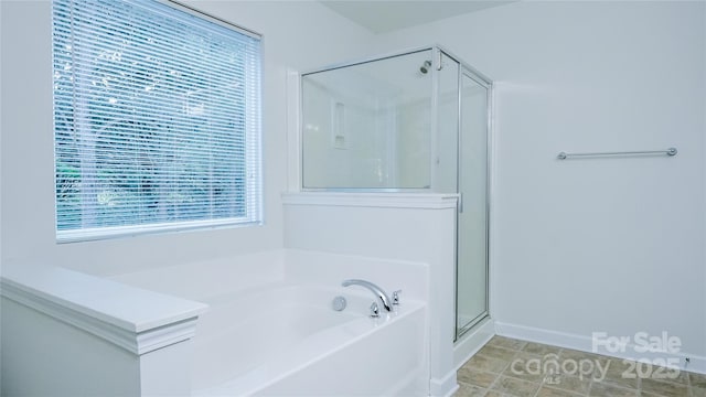 bathroom featuring baseboards, a stall shower, and a garden tub