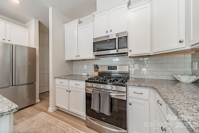 kitchen with backsplash, stainless steel appliances, white cabinetry, and light wood-type flooring