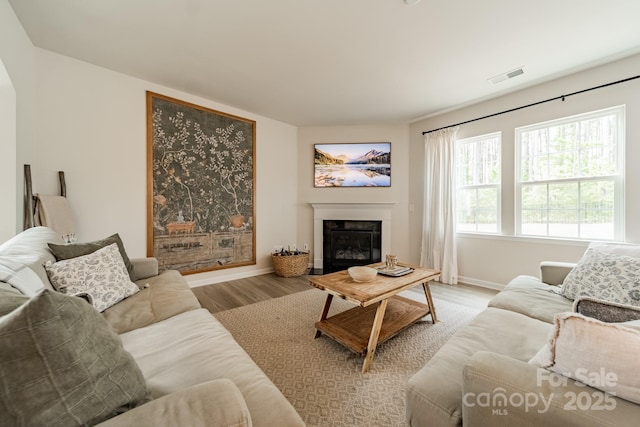 living room featuring baseboards, light wood-style floors, a glass covered fireplace, and visible vents