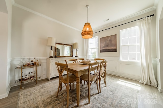 dining room with light wood-style floors, a decorative wall, crown molding, and wainscoting