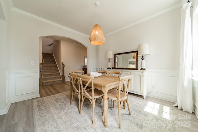 dining area with crown molding, arched walkways, stairway, a wainscoted wall, and light wood-style flooring