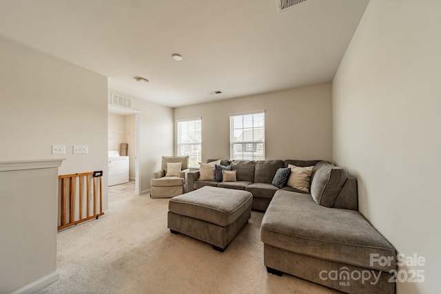 living room featuring washer / clothes dryer, light colored carpet, and visible vents