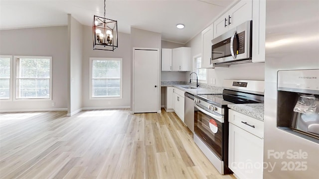 kitchen with a sink, light wood-type flooring, light stone countertops, a notable chandelier, and appliances with stainless steel finishes