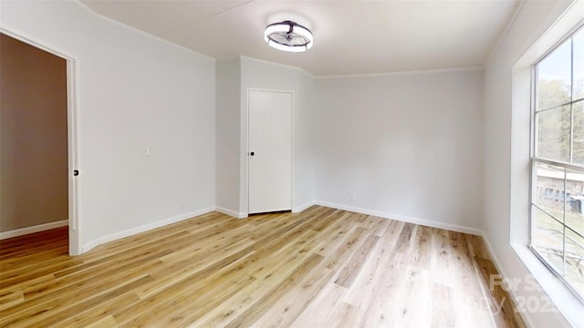 empty room with light wood finished floors, ornamental molding, and baseboards