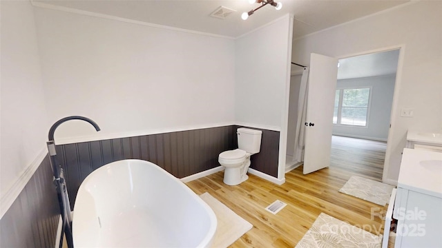 full bath with wood finished floors, a wainscoted wall, a soaking tub, visible vents, and vanity