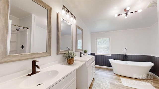 full bath with double vanity, wood finished floors, a sink, a wainscoted wall, and a soaking tub