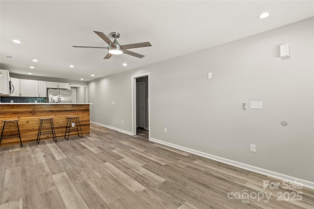 kitchen featuring stainless steel refrigerator with ice dispenser, a peninsula, baseboards, and light wood-style floors