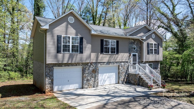 bi-level home with driveway, stone siding, and a garage