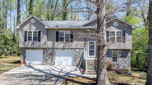 raised ranch with a garage, concrete driveway, and stone siding