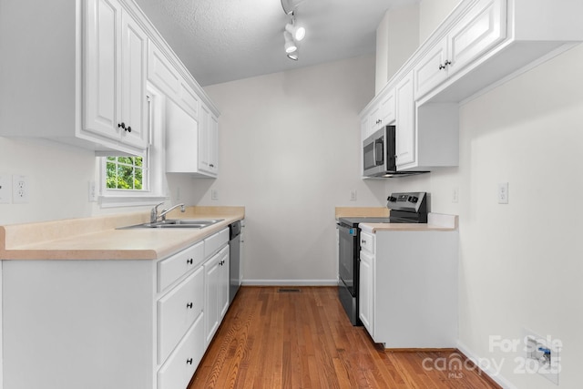 kitchen featuring wood finished floors, baseboards, white cabinets, a sink, and stainless steel appliances