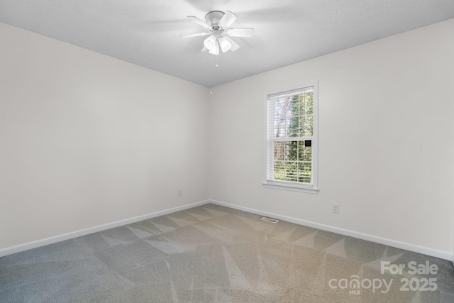 carpeted spare room with baseboards, a ceiling fan, and visible vents