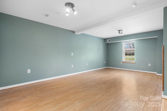 empty room with baseboards, light wood-style flooring, beam ceiling, and visible vents
