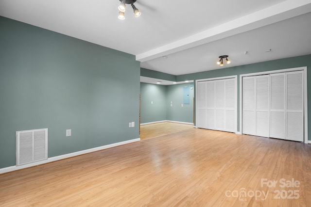 unfurnished bedroom featuring baseboards, multiple closets, visible vents, and wood finished floors