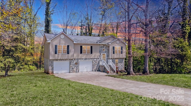 raised ranch featuring stone siding, a garage, stairway, a yard, and driveway