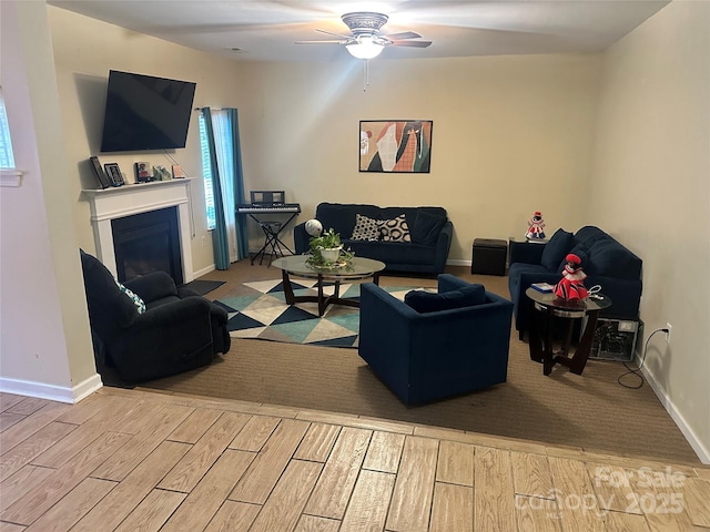 living room featuring baseboards, a ceiling fan, wood finished floors, and a fireplace with flush hearth