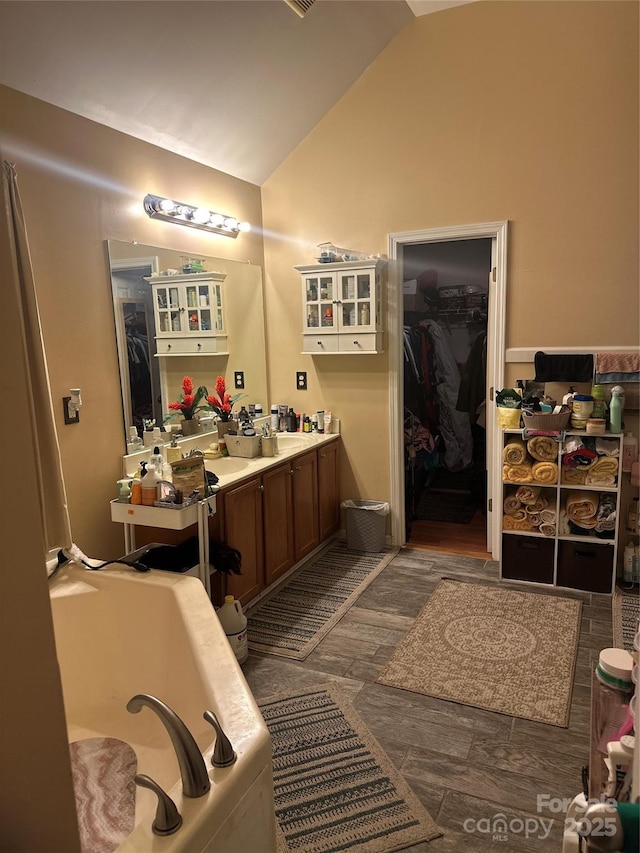 full bathroom with a walk in closet, vanity, a garden tub, and vaulted ceiling