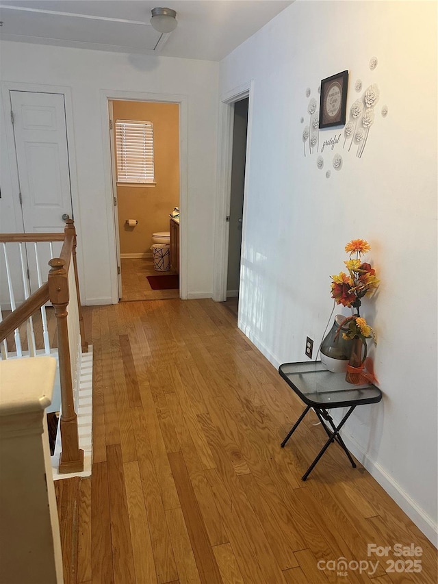 corridor with light wood-style floors, baseboards, and an upstairs landing