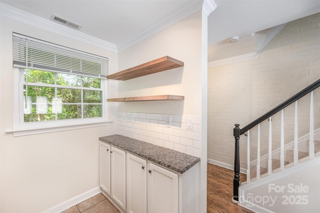 interior space featuring crown molding, visible vents, baseboards, and brick wall