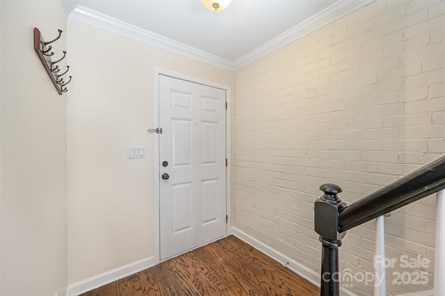 entrance foyer with brick wall, dark wood-type flooring, baseboards, and crown molding