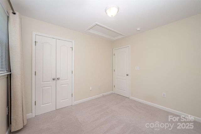 unfurnished bedroom featuring carpet floors, baseboards, attic access, and a closet