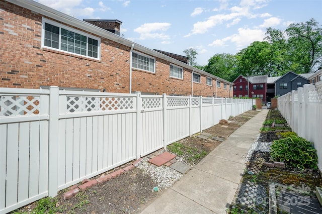 view of side of home featuring brick siding, a fenced backyard, and a chimney