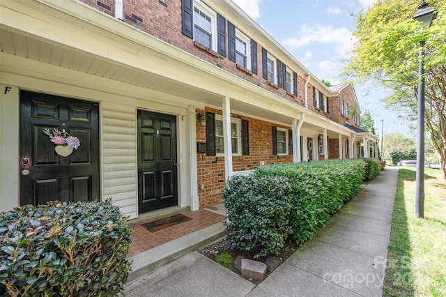entrance to property featuring a porch and brick siding