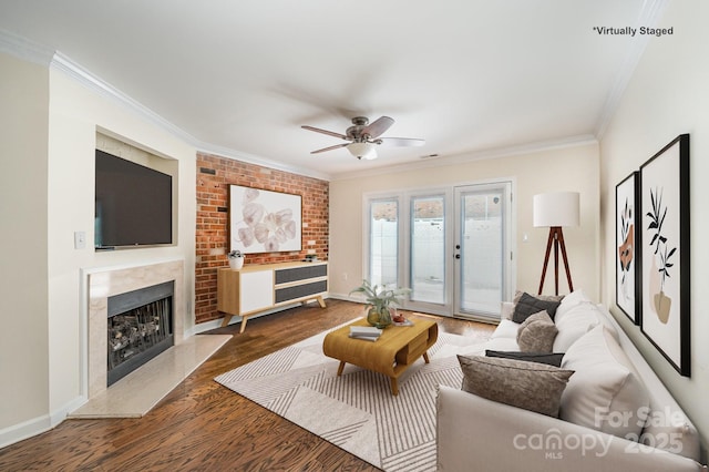 living area with wood finished floors, ornamental molding, baseboards, a fireplace, and ceiling fan