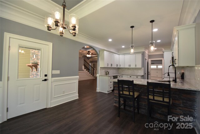 6519 Pargo Rd, Charlotte, NC 28216 - dining space with ornamental molding, stairs, dark wood-style floors, arched walkways, and a notable chandelier